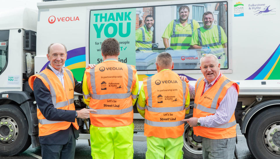 Two Veolia frontline operatives stand with their back to the camera showing off the StreetKind logo on their hi-vis vests which two colleagues either side point to it.