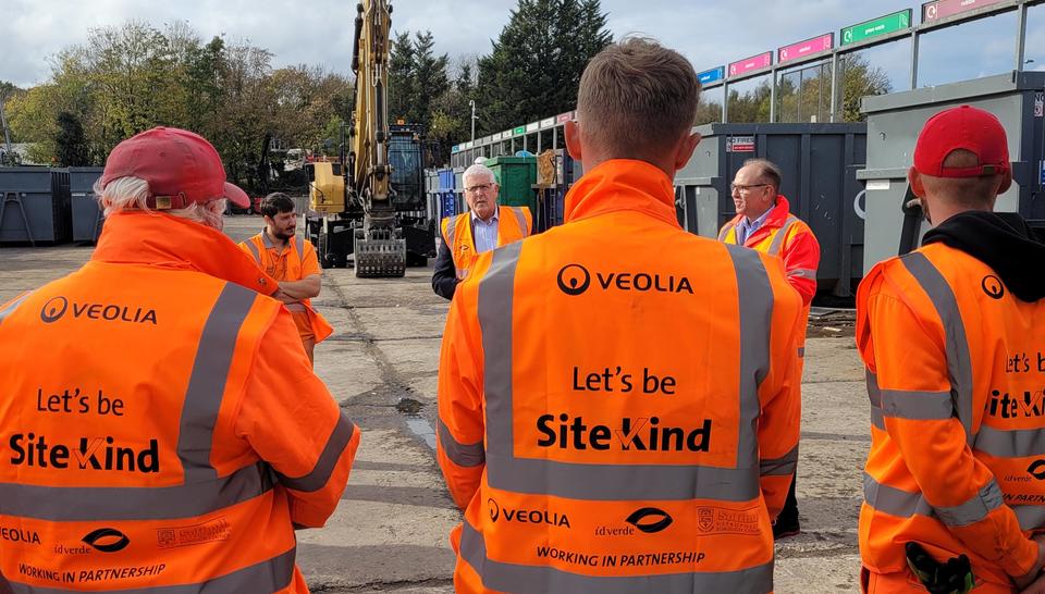 Veolia frontline colleagues stand with their backs to the camera showing the SiteKind logo on the back of their PPE.