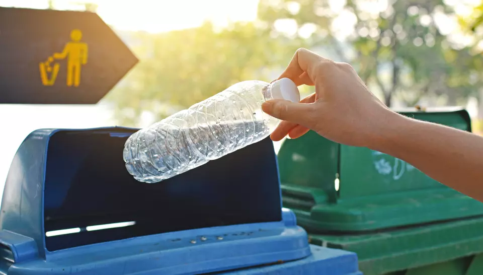 A hand places a plastic water bottle into a recycling bin.