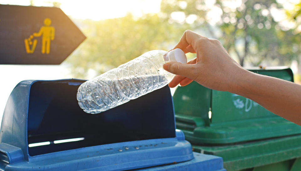 A hand places a plastic water bottle into a recycling bin.