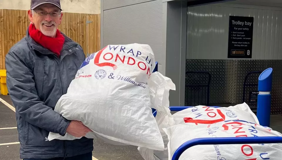 A man holds up a full bag of coats for donation.