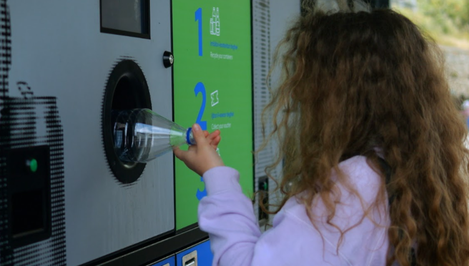 child pushing plastic bottle into recycling machine
