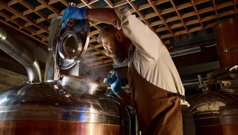 A man opening a still with steam escaping at a distillery or brewery plant