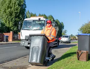 A loader wheels a bin down the road with a collection truck behind him.