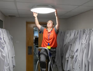 An engineer reaches up to fix a lightbulb.
