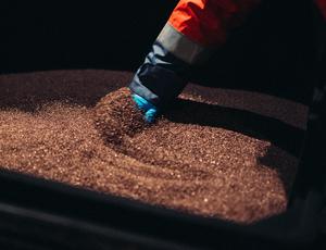 A gloved hand sifts through recycled copper.