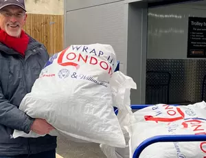 A man holds up a full bag of coats for donation.