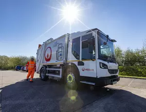 A Veolia operative walks in front of an RCV towards the driver's door.
