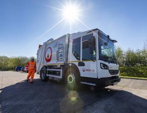 A Veolia operative walks in front of an RCV towards the driver's door.