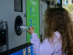 child pushing plastic bottle into recycling machine