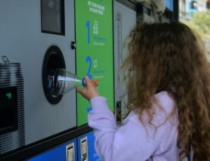 child pushing plastic bottle into recycling machine