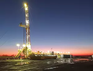 A large rig with a crane is lit up against a sunset background.