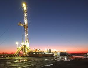 A large rig with a crane is lit up against a sunset background.