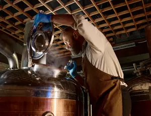 A man opening a still with steam escaping at a distillery or brewery plant