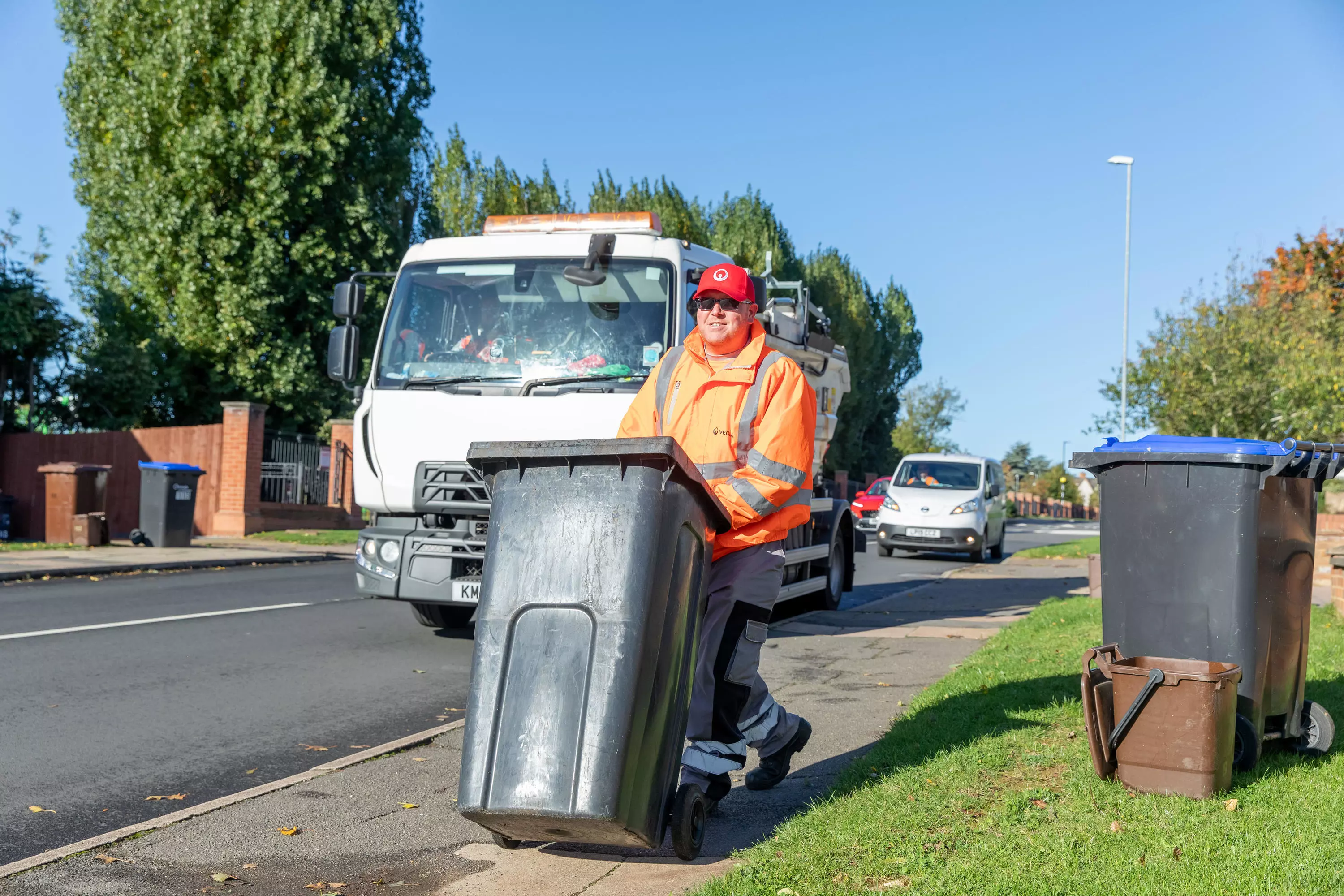 A loader wheels a bin down the road with a collection truck behind him.