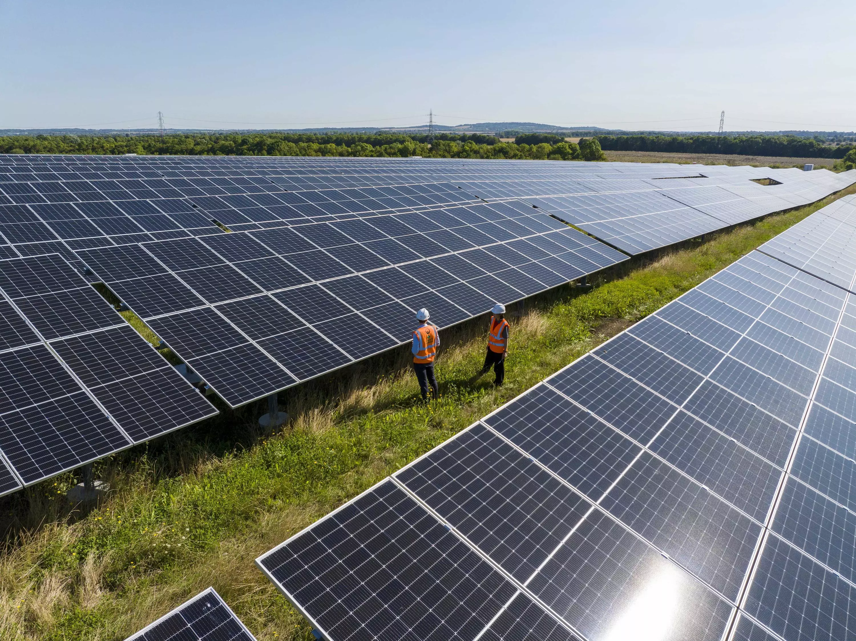 The image shows rows of solar panels with two people stood on the ground in between them.