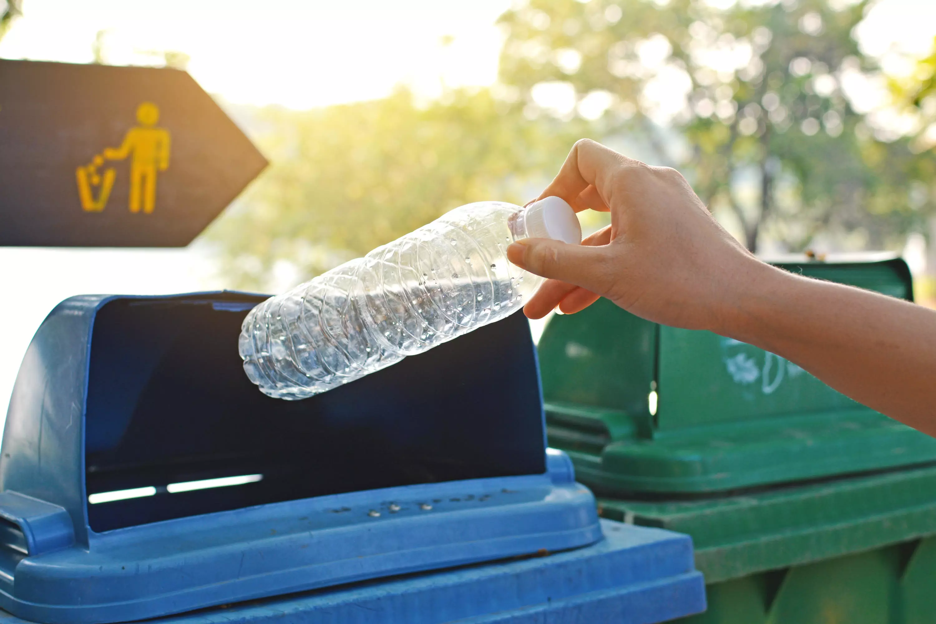 A hand places a plastic water bottle into a recycling bin.