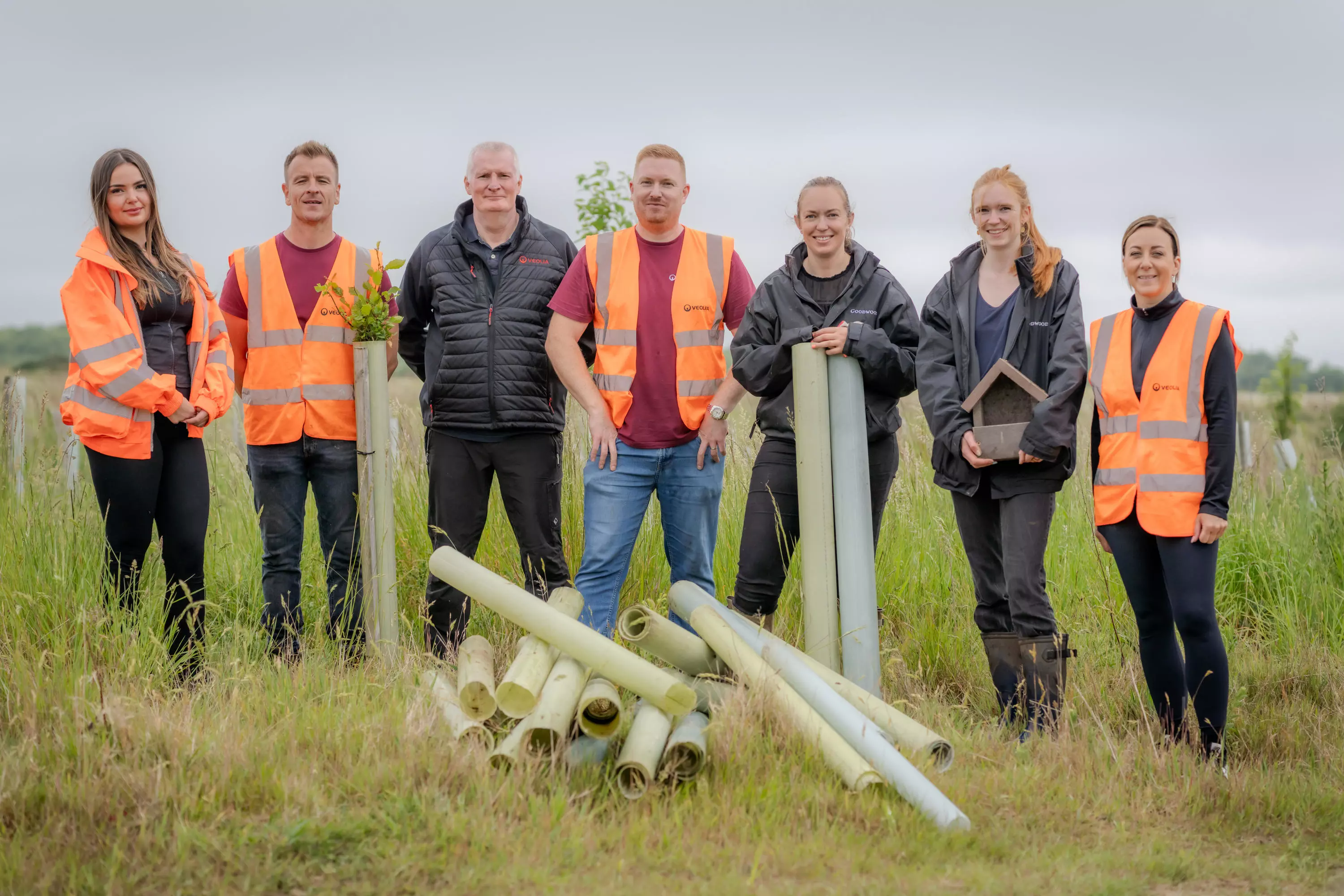 Veolia volunteers stand with the Goodwood Forestry Team behind a small pile of tree guards and smile at the camera.