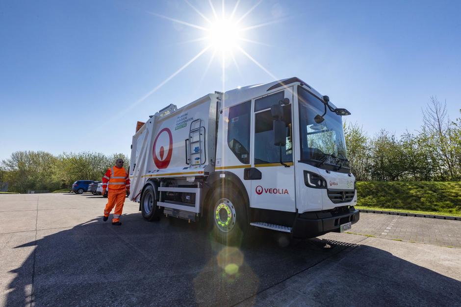 A Veolia operative walks in front of an RCV towards the driver's door.