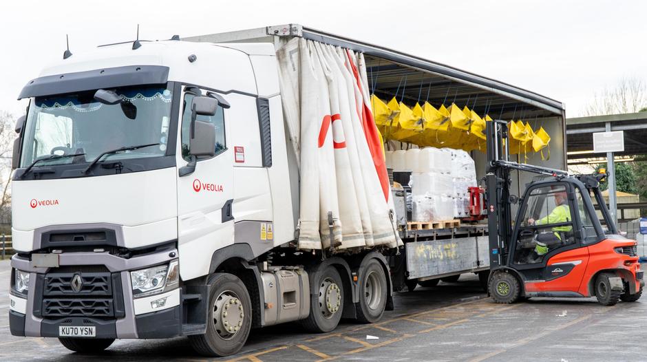 A forklift places a ballet onto the back of a Veolia truck.