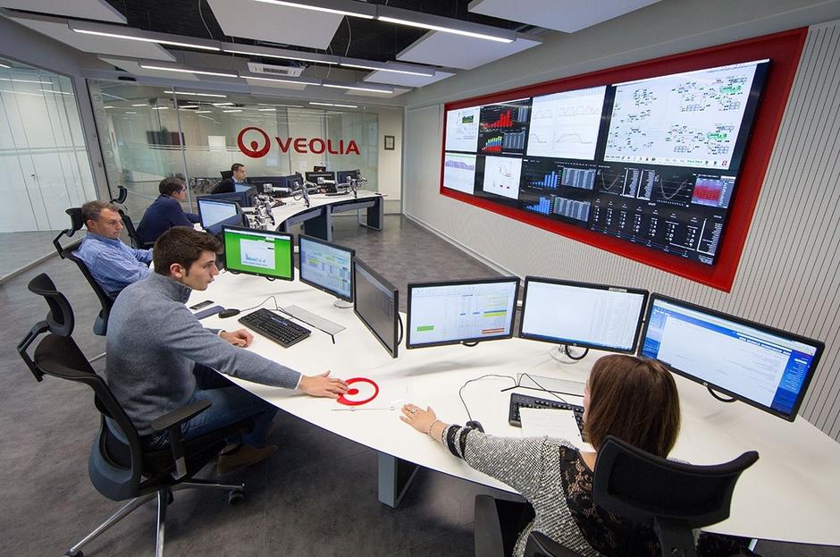 group of people sat around a large desk with computer monitors on