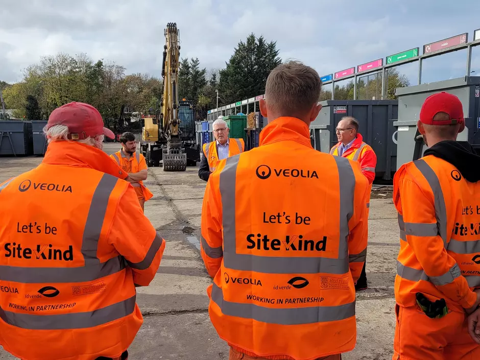 Veolia frontline colleagues stand with their backs to the camera showing the SiteKind logo on the back of their PPE.