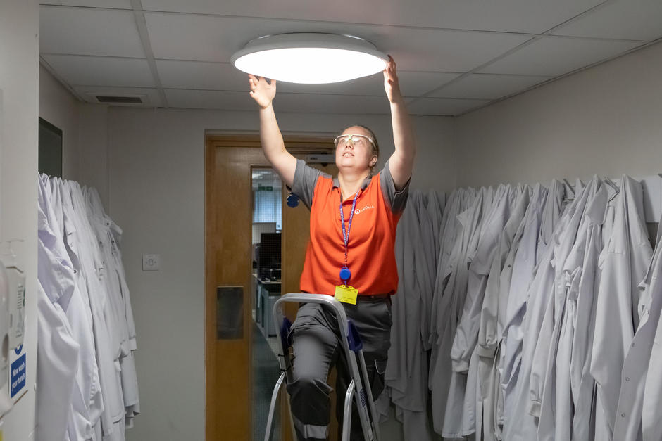 An engineer reaches up to fix a lightbulb.