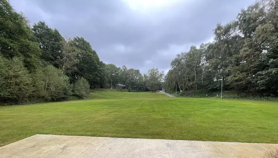 Photo of a green field with trees on either side.