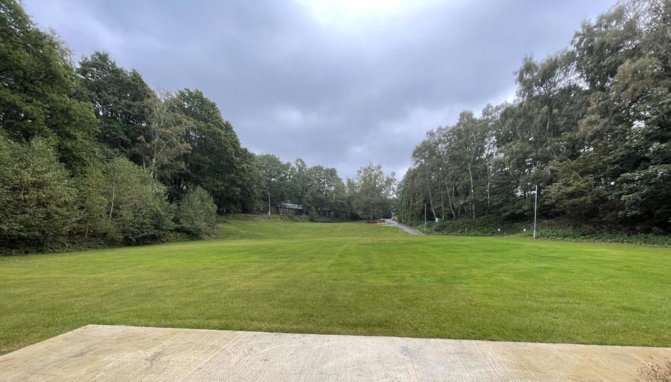 Photo of a green field with trees on either side.