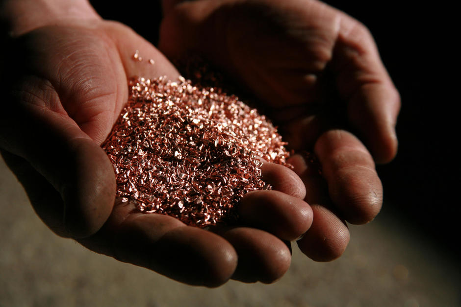 Hands hold a small pile of recycled copper flakes.