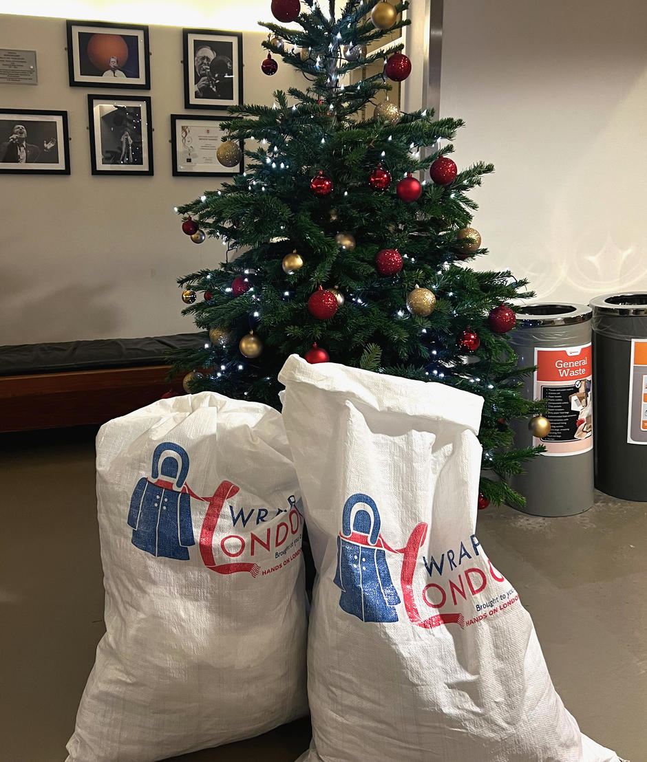 Two bags full of coats are propped up in front of a Christmas tree.
