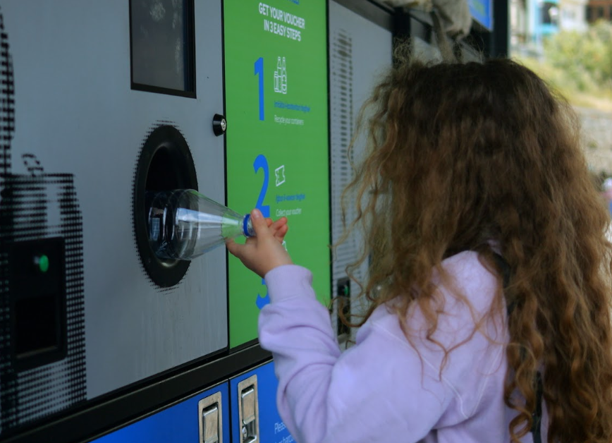 child pushing plastic bottle into recycling machine
