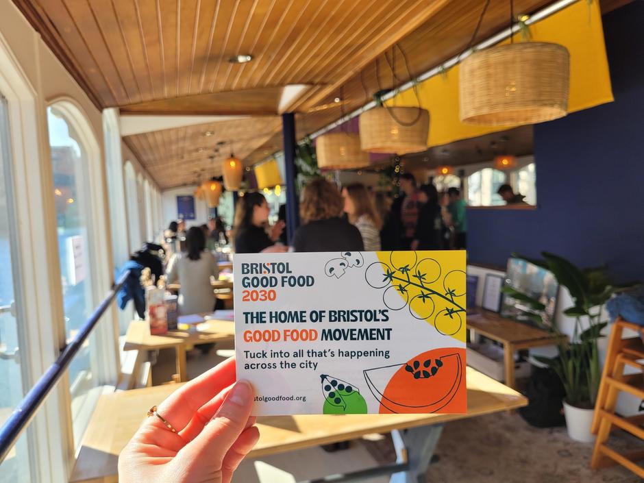 Image of a hand holding an A5 flyer with the Bristol Good Food logo on.