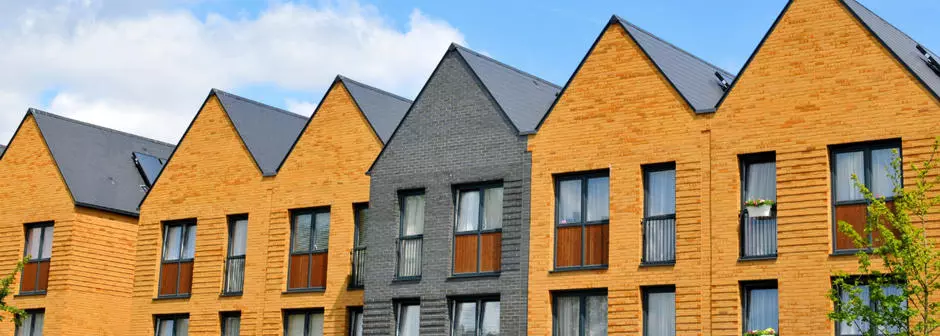 Photo taken of a row of terraced houses, all brown brick except for one grey house in the middle.