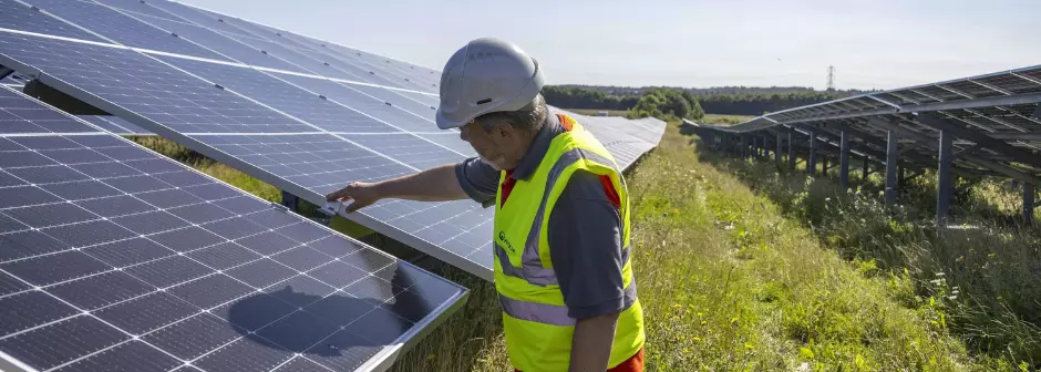 A Veolia operative checks on a solar panel, one of a long row in a green field.