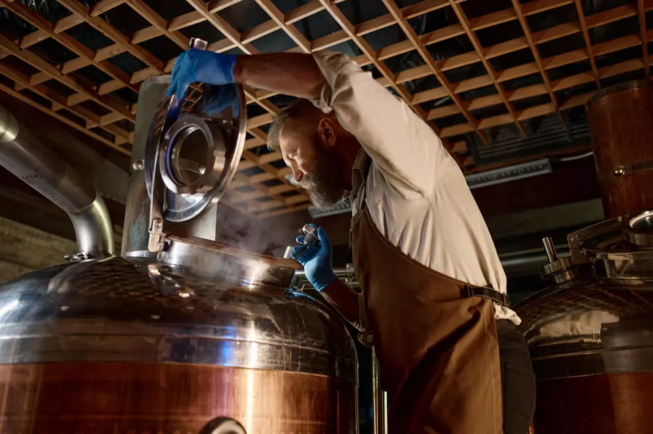 A man opening a still with steam escaping at a distillery or brewery plant