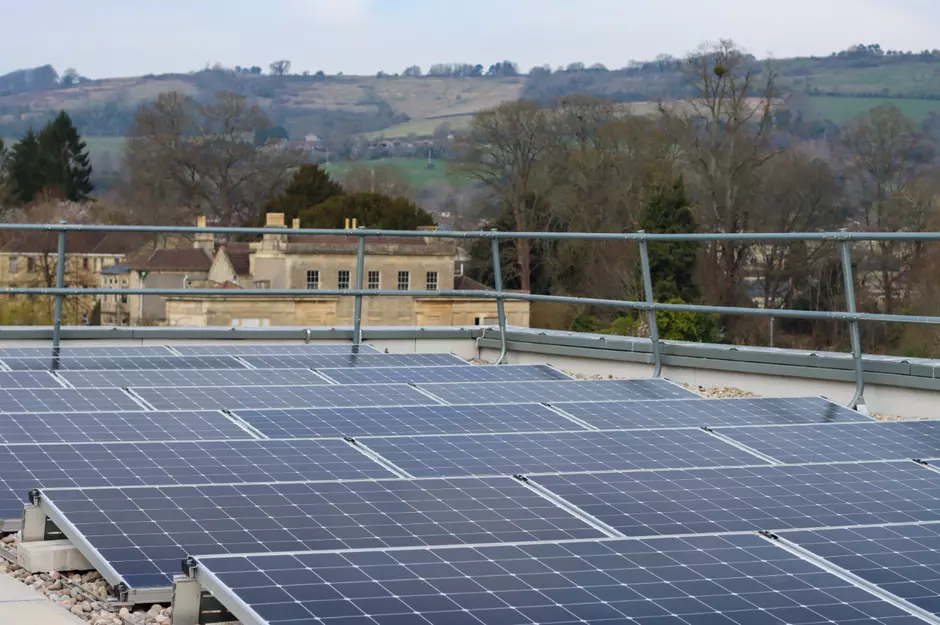 Photo taken from a rooftop looks out across a bank of solar panels with the rolling hills of Somerset and the iconic buildings of Bath in the distance.