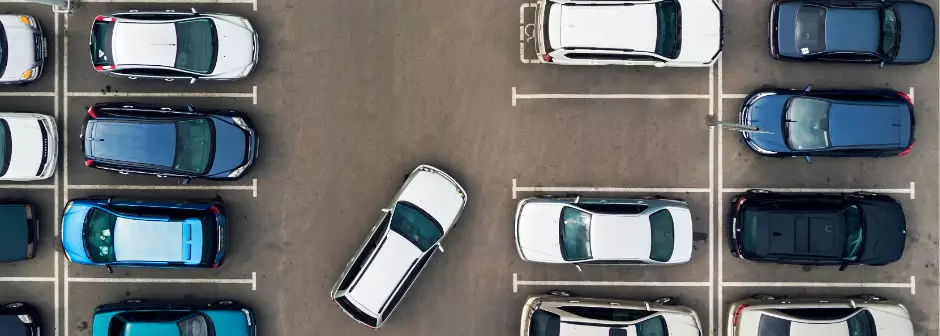 An aerial shot taken above a car park showing a car approaching an empty spot.