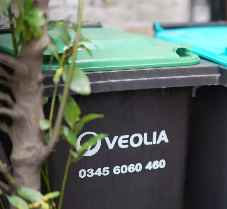 A black Veolia bin with white logo and green lid. 