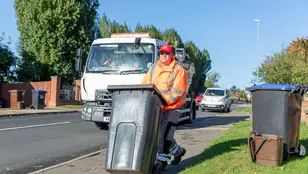 A loader wheels a bin down the road with a collection truck behind him.