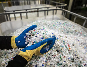 Image of gloved hands holding shredded plastics at a recycling facility